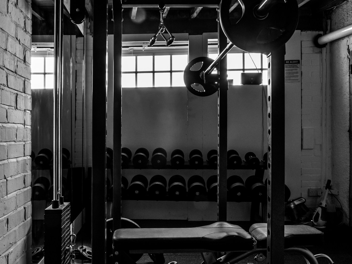 The training floor: rack, dumbbells and barbell in an old brick-walled gym